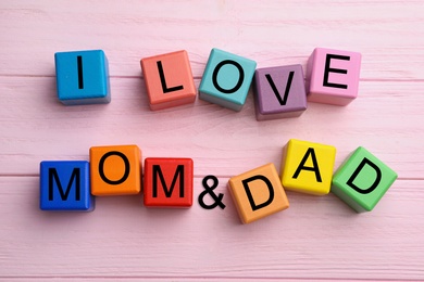 Photo of Words I LOVE MOM and DAD made from alphabet cubes on pink wooden table, flat lay