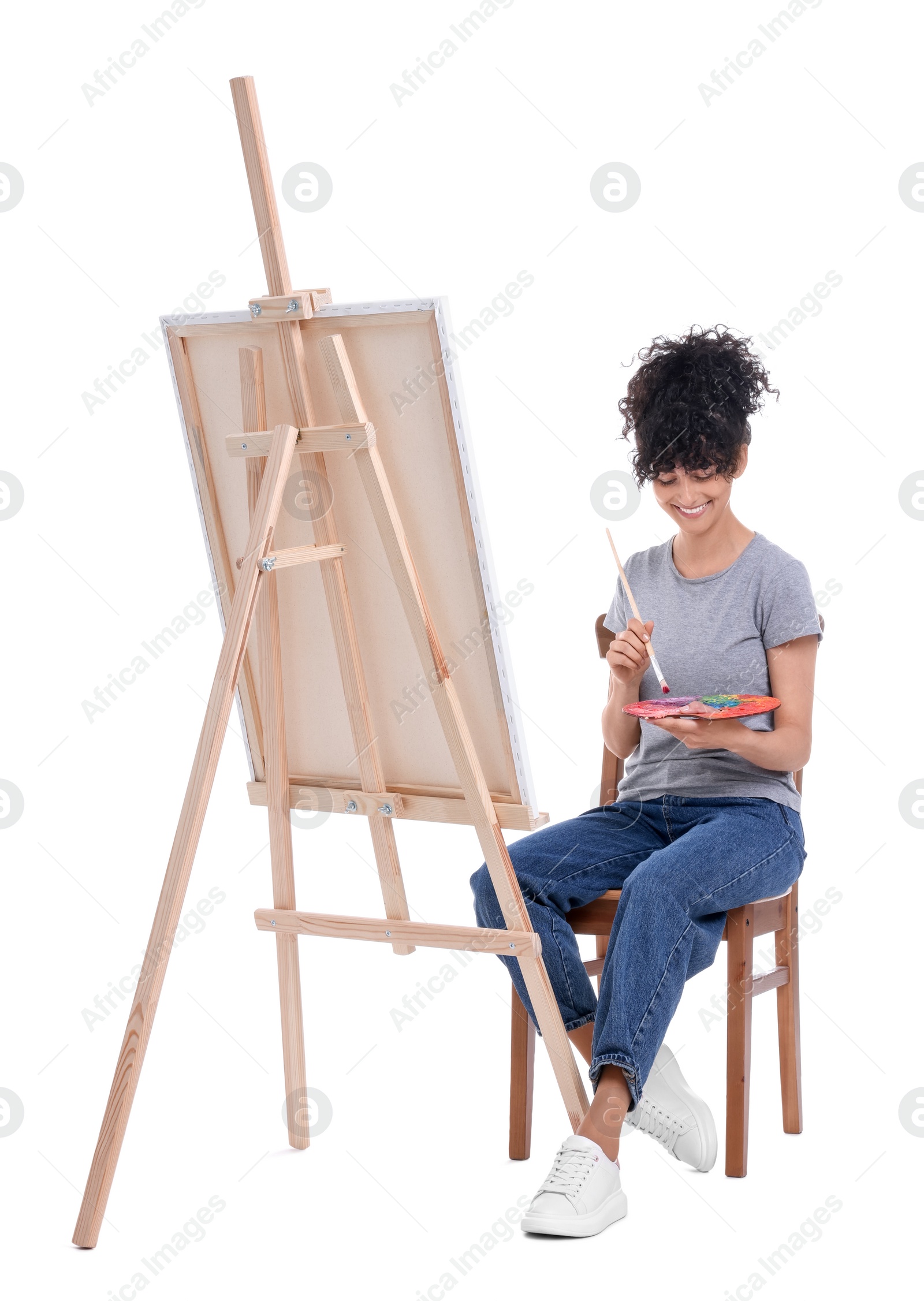 Photo of Young woman painting on easel with canvas against white background