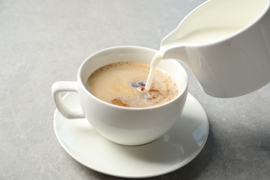 Pouring milk into cup of hot coffee on grey table