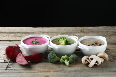 Photo of Different tasty cream soups in bowls and ingredients on old wooden table