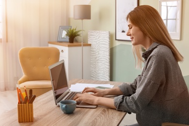 Photo of Young woman working with laptop at desk in home office