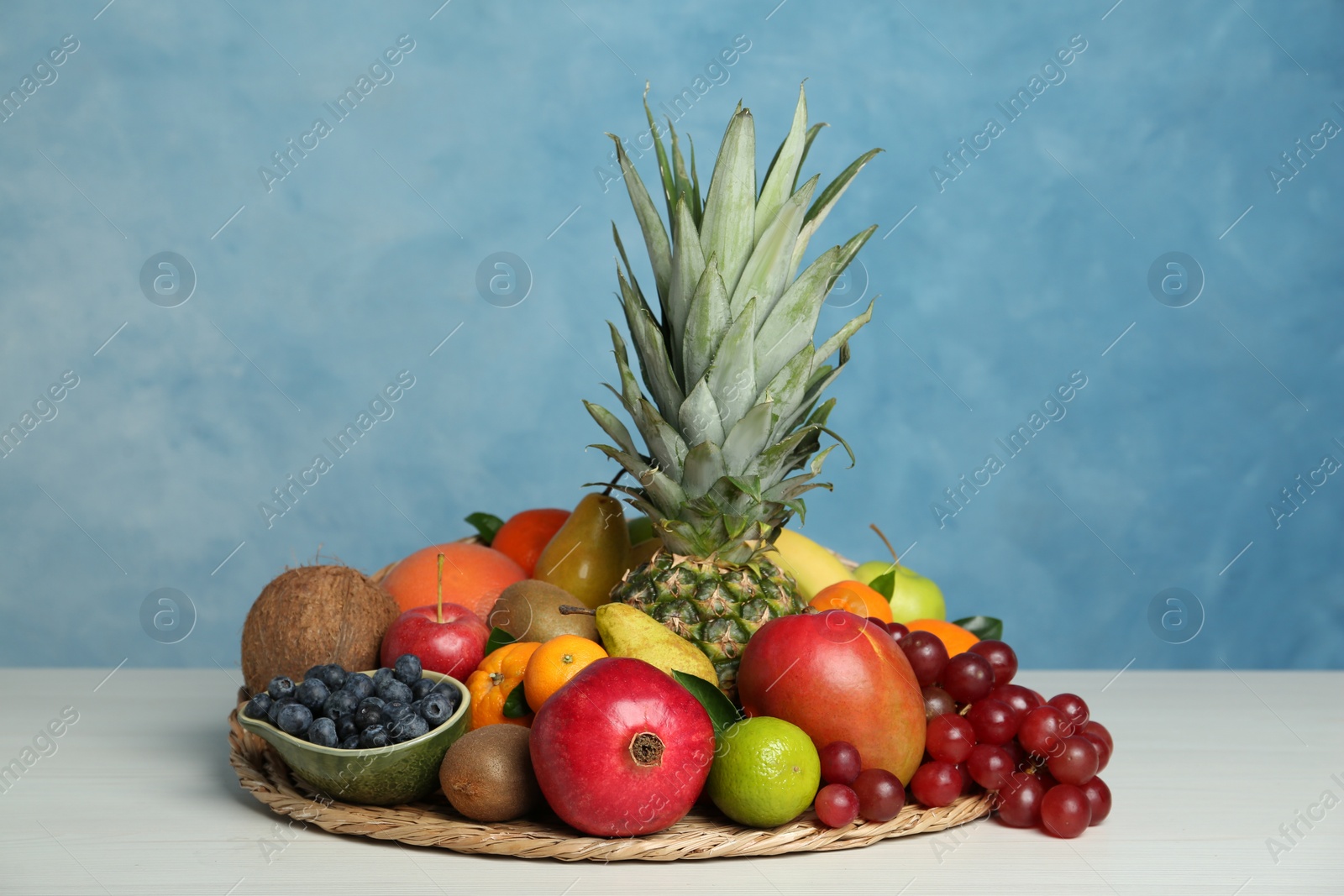 Photo of Assortment of fresh exotic fruits on white wooden table against light blue background