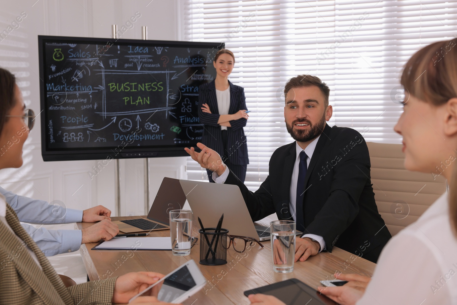 Photo of Business trainer near interactive board in meeting room during presentation, focus on colleagues