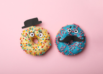 Photo of Funny faces made with donuts and paper on pink background, flat lay