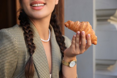 Photo of Smiling woman holding tasty croissant outdoors, closeup