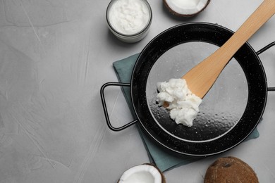 Photo of Frying pan with coconut oil and wooden spatula on light grey table, flat lay. Space for text