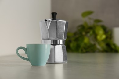 Ceramic cup and moka pot on light countertop in kitchen, space for text