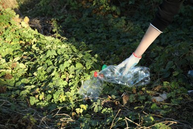 Photo of Woman picking up plastic bottle outdoors, closeup. Space for text