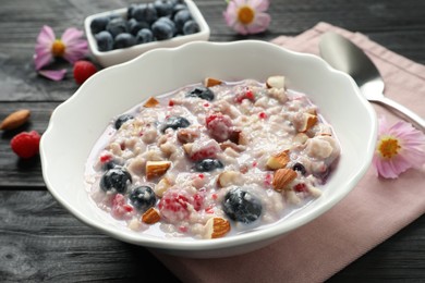 Photo of Tasty oatmeal porridge with toppings on black wooden table, closeup