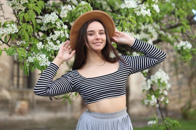 Photo of Beautiful woman in hat near blossoming tree on spring day