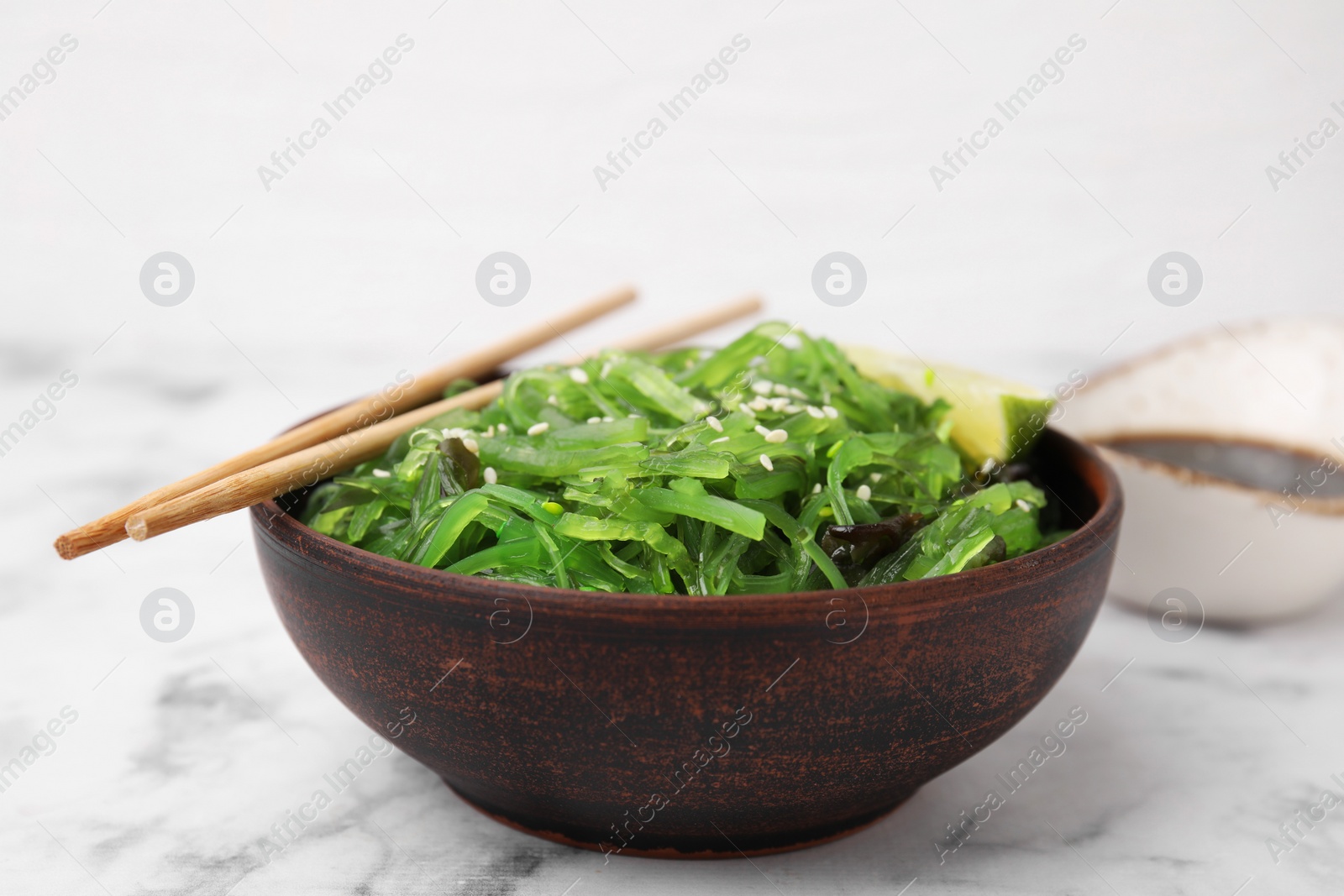 Photo of Tasty seaweed salad in bowl served on white marble table, closeup