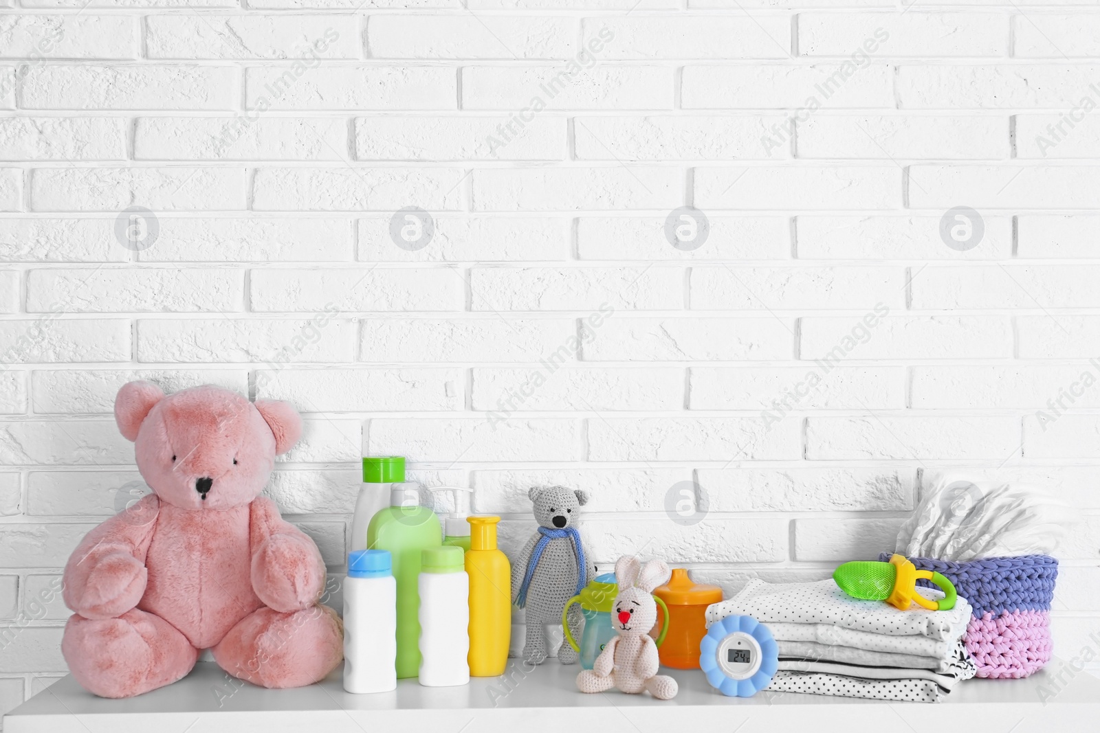 Photo of Baby accessories on table near white brick wall. Space for text