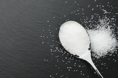 Granulated sugar and spoon on black table, top view. Space for text