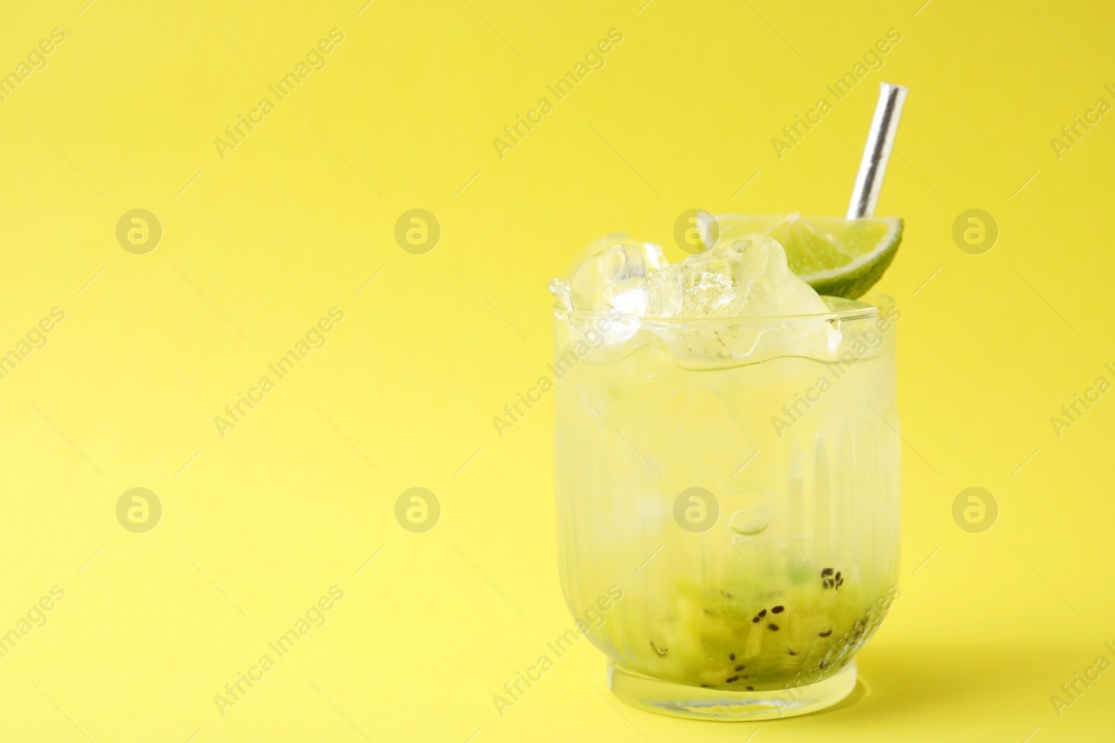 Photo of Glass of refreshing drink with kiwi and lime on yellow background, space for text