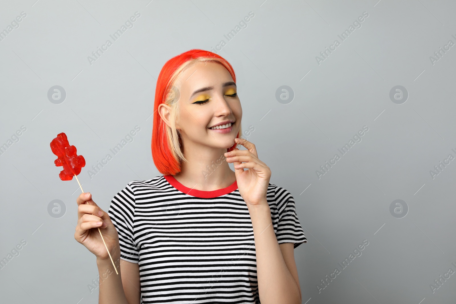 Photo of Beautiful young woman with bright dyed hair holding bear shaped candy on light grey background