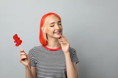 Beautiful young woman with bright dyed hair holding bear shaped candy on light grey background