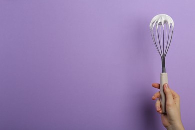 Photo of Woman holding whisk with whipped cream on violet background, closeup. Space for text
