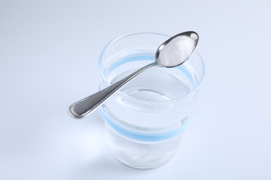 Photo of Glass of water and spoon with baking soda on white background