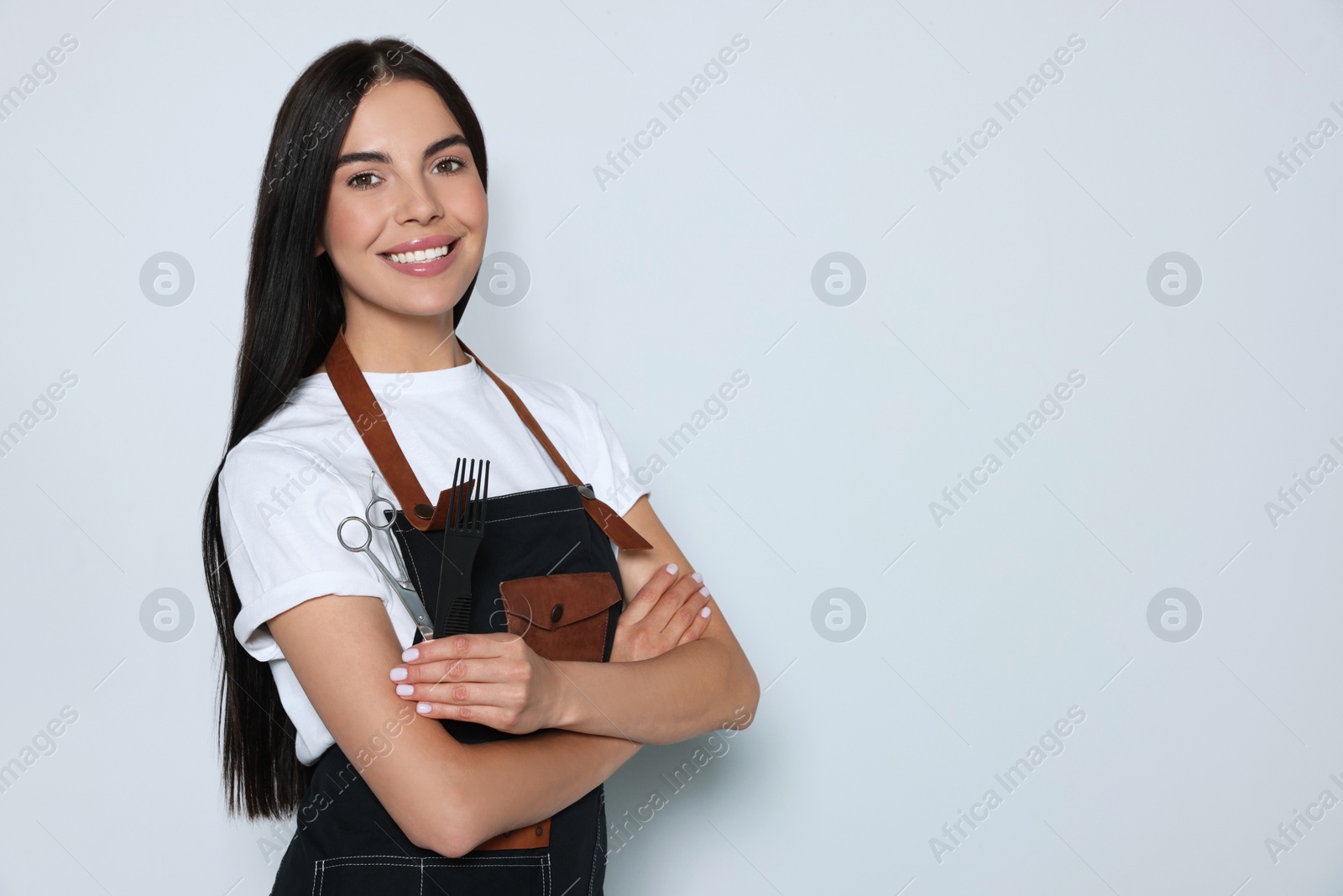Photo of Portrait of happy hairdresser with professional scissors and comb on light background, space for text