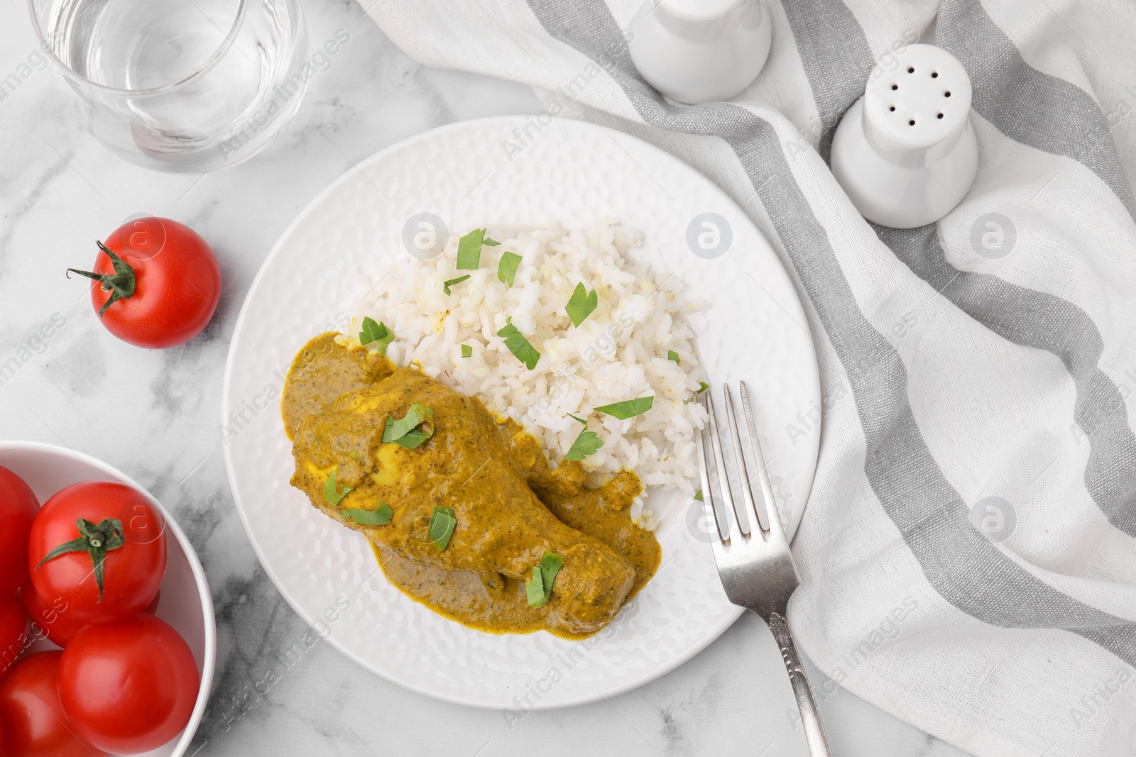 Photo of Delicious rice and chicken with curry sauce served on white marble table, flat lay