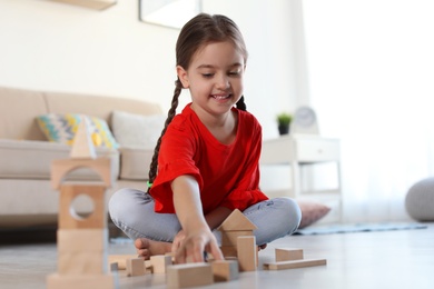 Photo of Cute little child playing with wooden building blocks on floor indoors
