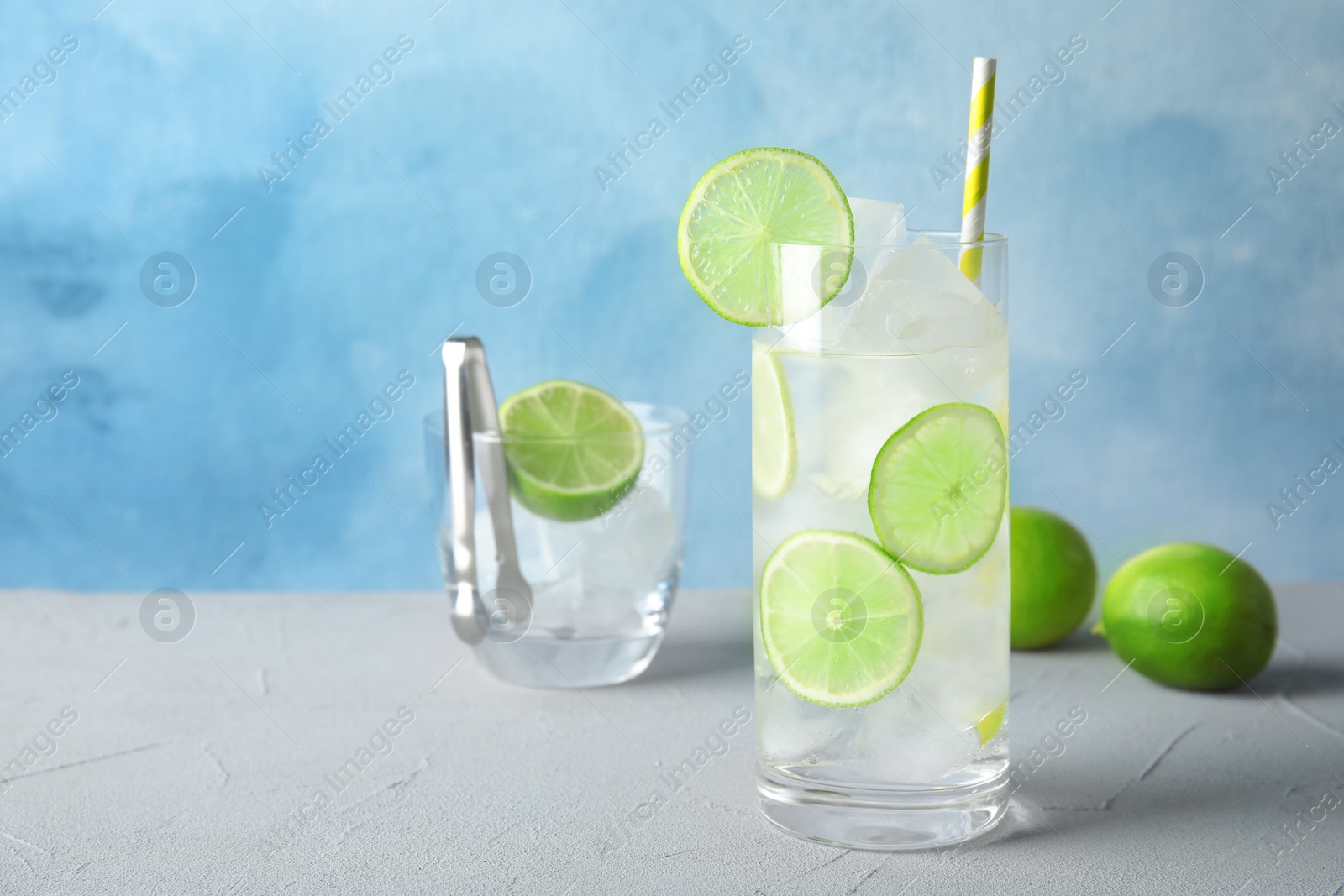 Photo of Glass of drink with lime and ice cubes on table against color background. Space for text