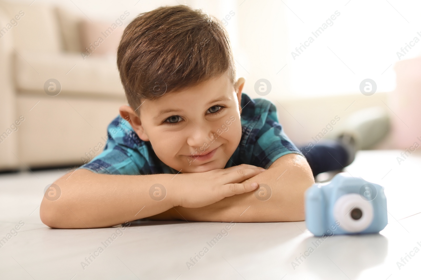 Photo of Little photographer with toy camera on floor at home