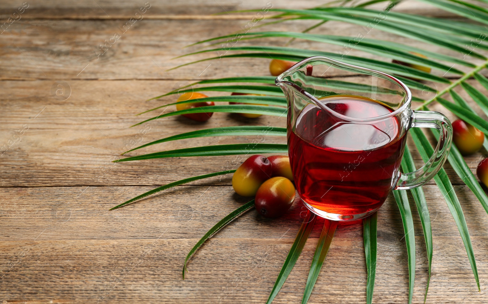 Photo of Palm oil in glass jug, tropical leaf and fruits on wooden table. Space for text