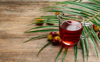 Palm oil in glass jug, tropical leaf and fruits on wooden table. Space for text