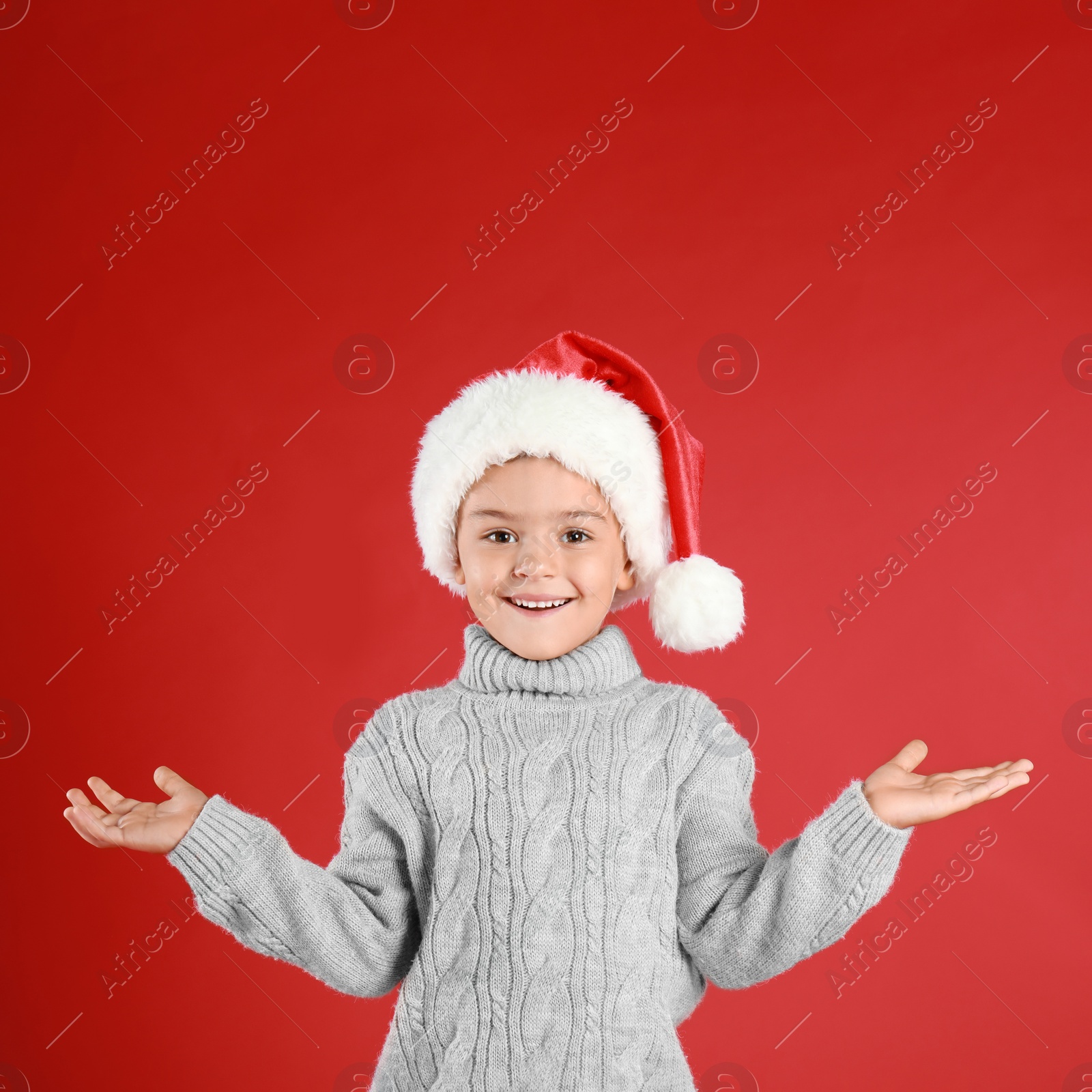 Photo of Cute little child wearing Santa hat on red background. Christmas holiday