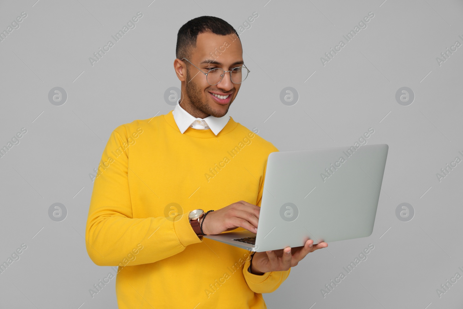 Photo of Happy young intern working on laptop against light grey background