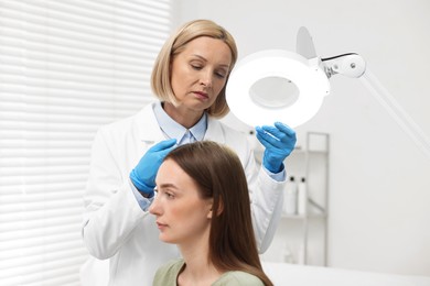 Trichologist examining patient`s hair under lamp in clinic