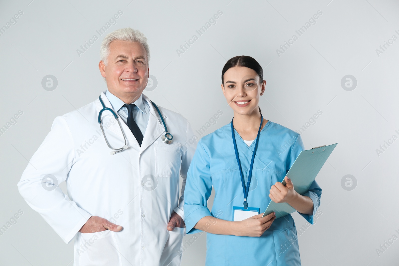 Photo of Senior doctor and young nurse against light background