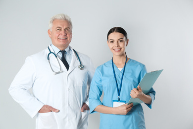 Photo of Senior doctor and young nurse against light background