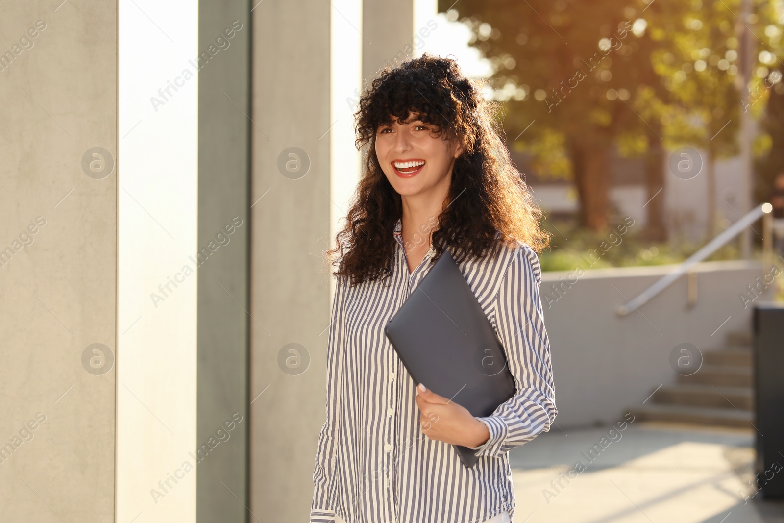 Photo of Happy young woman holding modern laptop outdoors