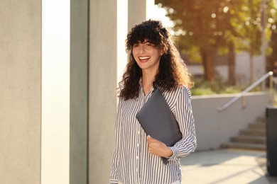 Photo of Happy young woman holding modern laptop outdoors