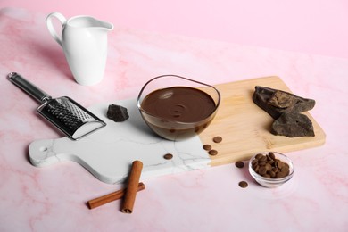 Bowl with tasty melted chocolate, pieces and cinnamon sticks on pink marble table