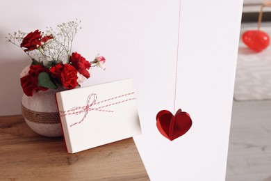 Photo of Vase with beautiful flowers and gift box on wooden table in room. Happy Valentine's Day
