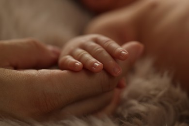 Mother holding hand of her newborn baby on fluffy blanket, closeup. Lovely family