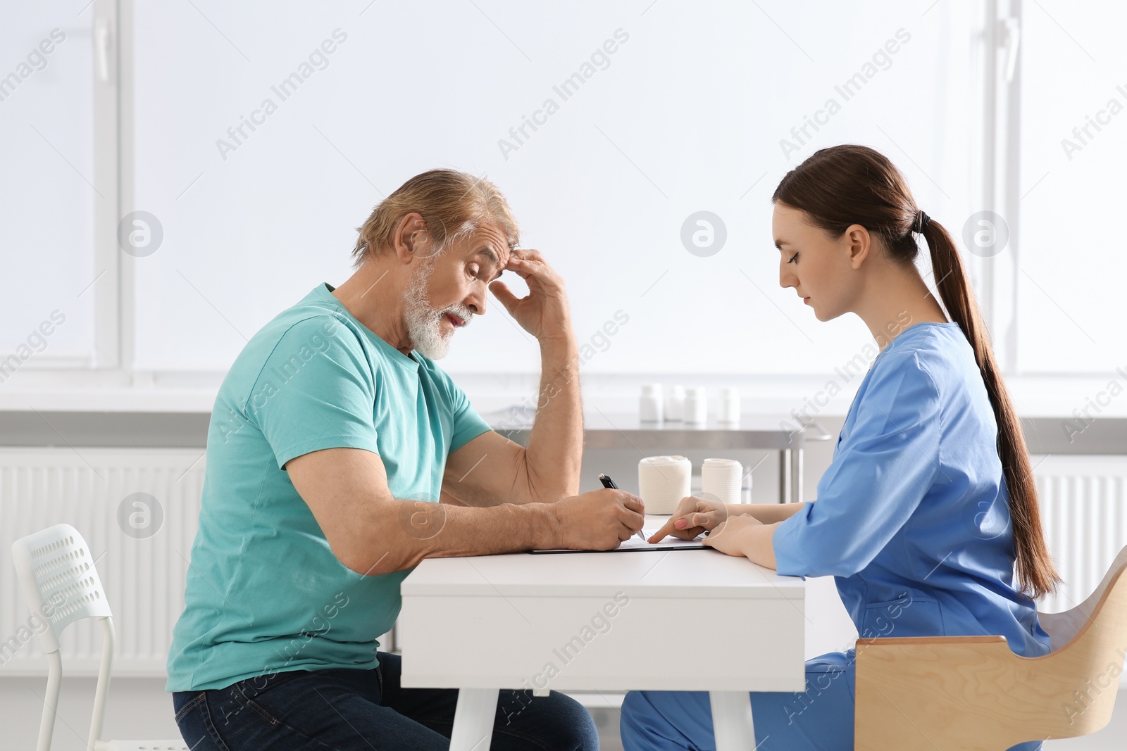 Photo of Doctor helping patient filling his medical card at table in clinic