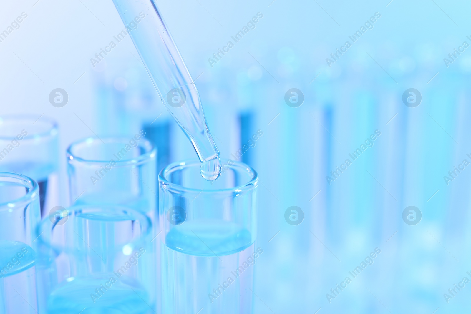 Photo of Dripping liquid from pipette into test tube on light blue background, closeup