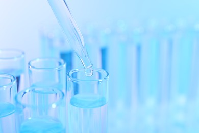 Dripping liquid from pipette into test tube on light blue background, closeup