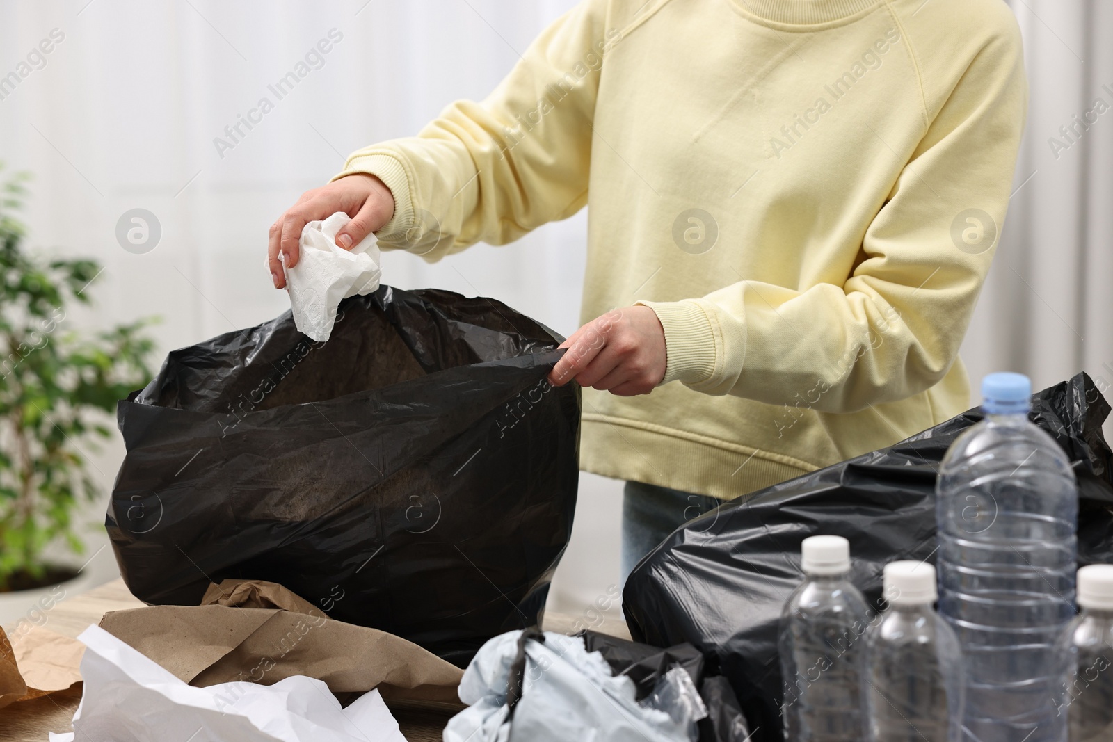 Photo of Woman with plastic bag separating garbage in room, closeup