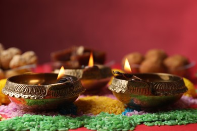 Diwali celebration. Diya lamps and colorful rangoli on red table, closeup