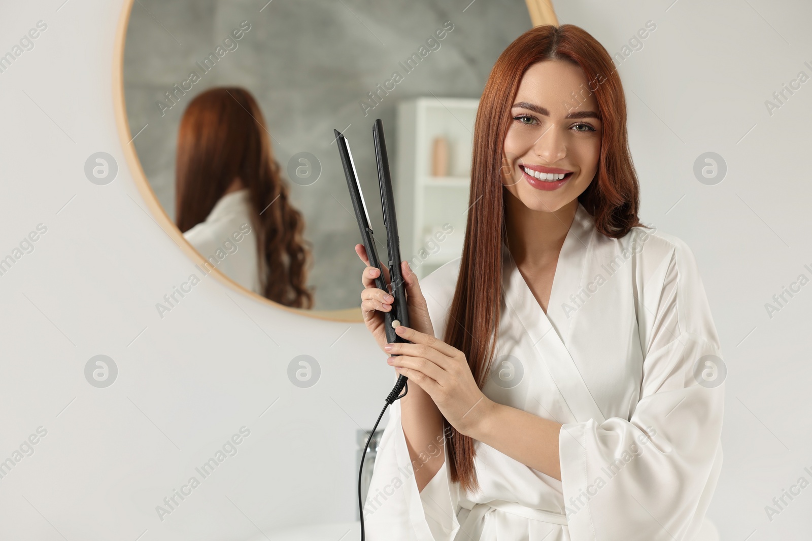 Photo of Beautiful woman with hair iron in room, space for text