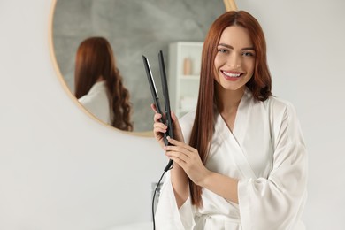 Beautiful woman with hair iron in room, space for text