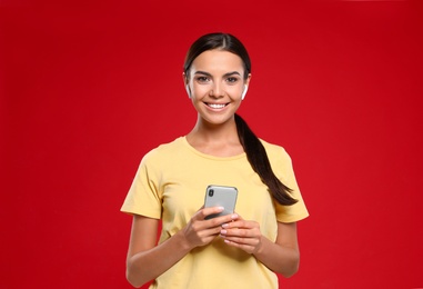 Happy young woman with smartphone listening to music through wireless earphones on red background