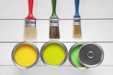 Cans of yellow and green paints with brushes on white wooden table, flat lay