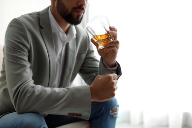 Photo of Young man with glass of whiskey at home, closeup. Space for text