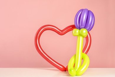 Photo of Flower and heart figures made of modelling balloons on table against color background. Space for text